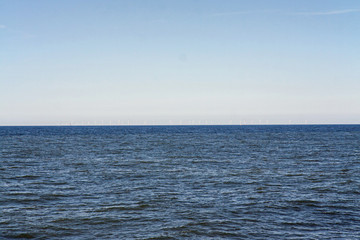 Obraz premium An offshore wind farm in the North Sea, barely visible on the horizon, just off the coast of the Netherlands, on a clear day.