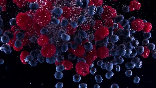 Blueberries and raspberries falling down in to the water. Lots of berries falling slowly on a black background. Organic forest fruit  isolated on black background. Fresh water with fruits.