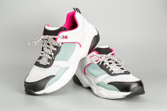 Weisse Damen-Sneaker mit hellblauen und rosaroten Akzenten. Mit grauem Hintergrund.