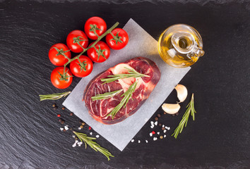 raw meat beef steak with bone on paper and black slate background. top view, flat lay.