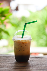 Iced coffee latte in plastic cup on wooden table and nature green background - iced drinks