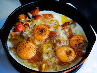 Scrambled eggs with tomatoes are fried in a cast-iron pan on an induction electric stove