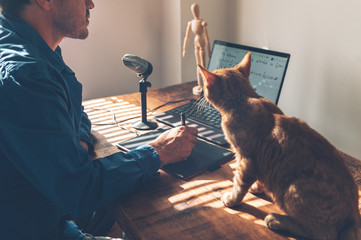 Young university professor is doing online lecture for his students from home during lockdown. He is using laptop and graphic tablet and is writing math formulas with stylus pen