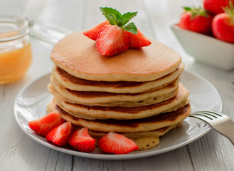 Close-up of a pile of fresh homemade pancakes with butter, honey and strawberries on a white wooden background. Traditional American, rustic breakfast