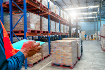 The  man holding tablet to checking the stock products,Employee using warehouse software to...