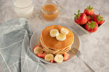 Top view of pancakes decorated with pieces of butter and fruit, glass of milk and copper Traditional American breakfast, place for text