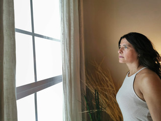 Woman looks out the window of her home opening the curtains in a home environment