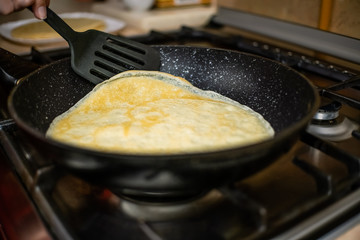 woman's hand turns a pancake with a black spatula on a frying pan close-up. concept of Breakfast