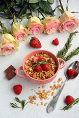 Bowl with cereal, strawberries, spoon, chocolate and roses on a light background, top view