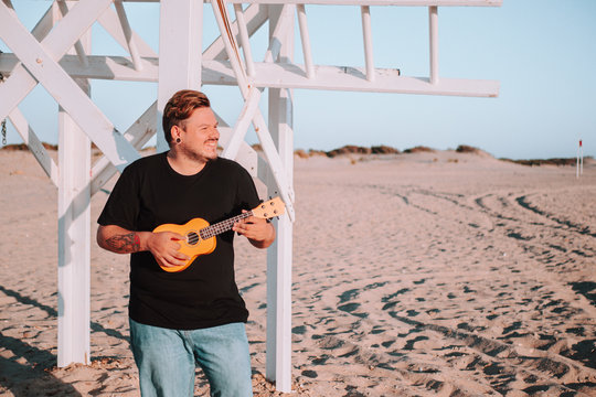 Hombre joven tocando el ukelele en la playa bajo la luz del sol durante la puesta de sol