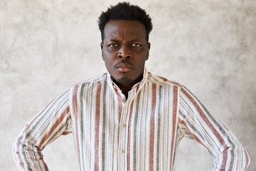 Negative human emotions and reactions. Sullen gloomy young African man standing in tense posture...