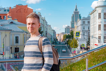 A young man with a backpack stands with a background on a business street in Moscow 