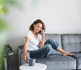 Portrait of a beautiful young female sitting on a sofa in a white t-shirt with a charming smile,...