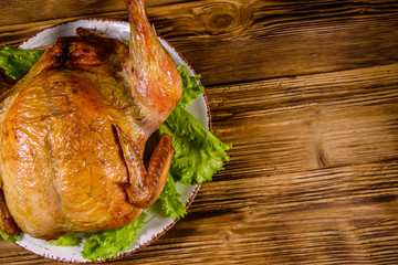 Plate with roasted whole chicken and lettuce leaves on a wooden table. Top view