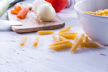 Macaroni on white background with onion, tomato and garlic on a wooden table in background. Close up view.