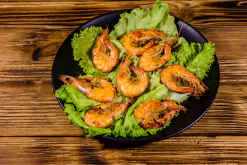 Plate with grilled shrimps and lettuce leaves on a wooden table