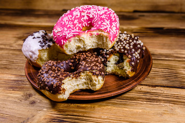 Plate with bitten glazed donuts on a wooden table