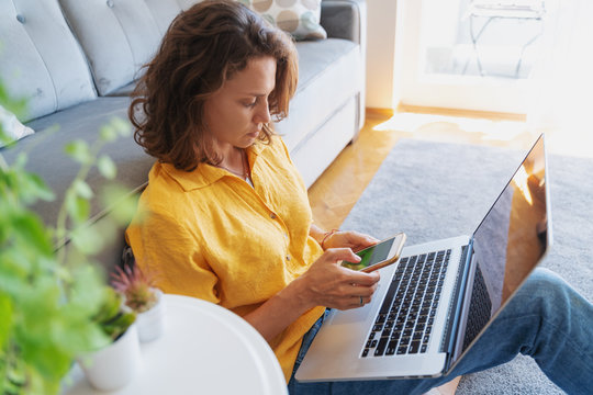 A Beautiful Young Femal In A Yellow Shirt Sits On The Floor On A Carpet With A Laptop, Freelancer And Home Office Concept. Work From Home