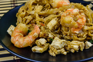Black plate with pad thai on a bamboo mat