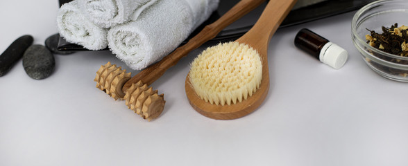  SPA Background for a banner with wellness items. Brush for dry body massage. Wooden massager for face and body. Wet white towels on a black ceramic dish. Sea pebbles and aromatic oil. Copy space