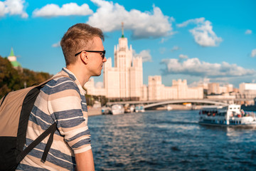 Fototapeta na wymiar Portrait of a young blond man with the background of the famous high-rise building and the Moscow river on a Sunny summer day