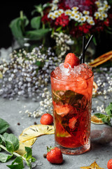 Strawberry Mojito. Cold summer mojito cocktail with strawberries, mint, lemon and ice in a glass on a table. on a dark background