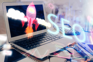 Double exposure of table with computer and seo drawing hologram. Search optimization concept.