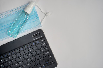 Tablet keyboard next to mask, disinfectant on grey background with space on the right for text