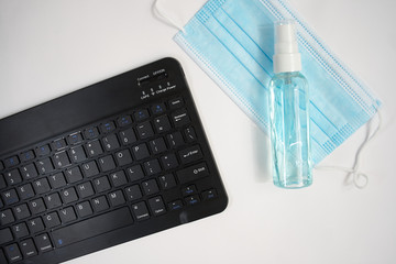 Tablet keyboard next to mask, disinfectant on grey background