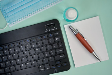 Tablet keyboard next to mask ,disinfectant ,note block,pencil and reading point on green background