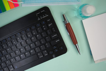 Tablet keyboard next to mask ,disinfectant,block notes and pencil on green background