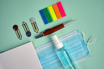 Mask, disinfectant, notepad, reading point, clips and portaminas on green background