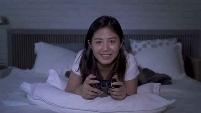 closeup japanese young female lying prone on bed, talking to herself while playing console games at midnight. teenage girl addicted to video games. indoor recreation and authentic lifestyle