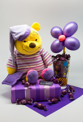 toy Teddy bear on a white background in purple tones with a flower from balloons on the gift and with candy