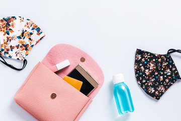 Woman purse with fashionable face masks, hand sanitizer, smartphone and cosmetics on white table...
