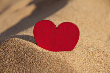 wooden red heart in golden sand on sunny beach, copy space