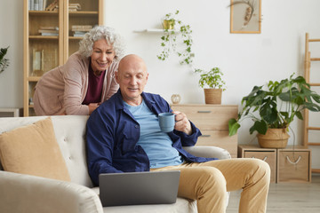 Portrait of modern senior couple smiling at laptop camera during video call with family, copy space