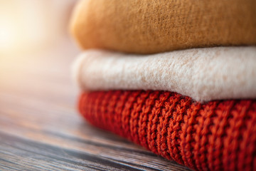 Obraz na płótnie Canvas Pile of knitted woolen sweaters autumn colors on wooden table. Clothes with different knitting patterns folded in stack. Warm cozy winter fall knitwear concept. Copy space.