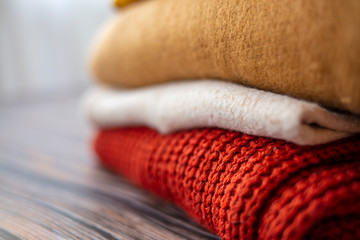 Pile of beige woolen clothes on a wood background. Warm knitted sweaters and scarfs are folded in one heap. Autumn clothes. Knitted wool sweaters