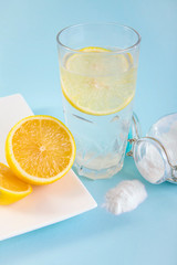 Baking soda in drinking glass with water and lemon slice juice, health benefits for digestive system concept. Light blue background.