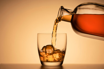 a glass of whiskey on the rocks. pouring Bourbon or cognac from a liquor bottle. orange background