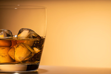 glass of whiskey on the rocks ice close-up. or other alcohol: Bourbon, cognac, or liqueur. Orange background, free space for text, copy space.