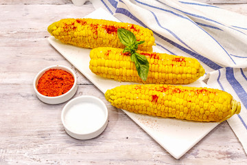 Boiled corn cobs on ceramic plate. Sea salt, fragrance paprika, fresh basil leaf