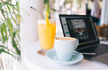 Cropped image of mug with coffee and orange juice for french breakfast near laptop computer on...