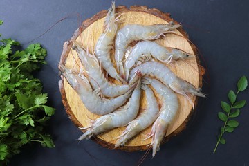 fresh shrimps or white prawns raw on wooden chopping board with coriander and curry leaves. on background with copy space.