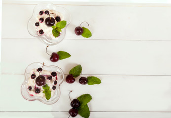 Naklejka na ściany i meble Whipped cream with cherries, currants and mint leaves in glass bowls, bowls, scattered berries on a light background. Copy spaes. horizontally