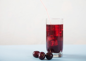 A glass of cherry juice with ice and cherries on a white table. Copy spaes.