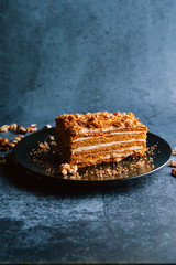 Slice of brown walnut cake in a black plate. Walnuts around the cake as side decoration. Delicious cake and sweets.
