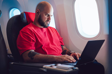 Young man browsing laptop during flight by airplane