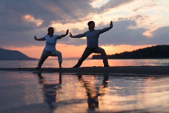Man and woman doing Tai Chi chuan at sunset on the beach.  solo outdoor activities. Social Distancing. Healthy lifestyle  concept. 